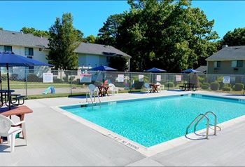 A swimming pool with chairs and umbrellas in front of houses 
